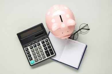 Photo of Calculator, piggy bank, notebook and glasses on light grey background, flat lay