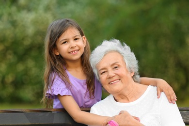 Photo of Little girl and her grandmother hugging on bench in park