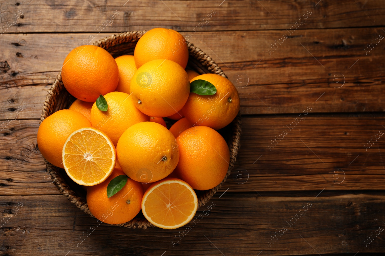 Photo of Many ripe oranges and green leaves on wooden table, top view