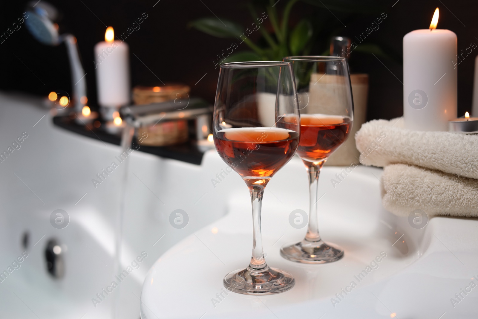 Photo of Bathtub with glasses of wine and candles indoors. Romantic atmosphere