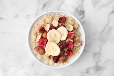 Delicious oatmeal with freeze dried berries, banana and hazelnuts on white marble table, top view