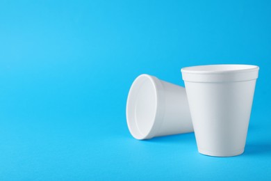 Photo of White styrofoam cups on light blue background, space for text