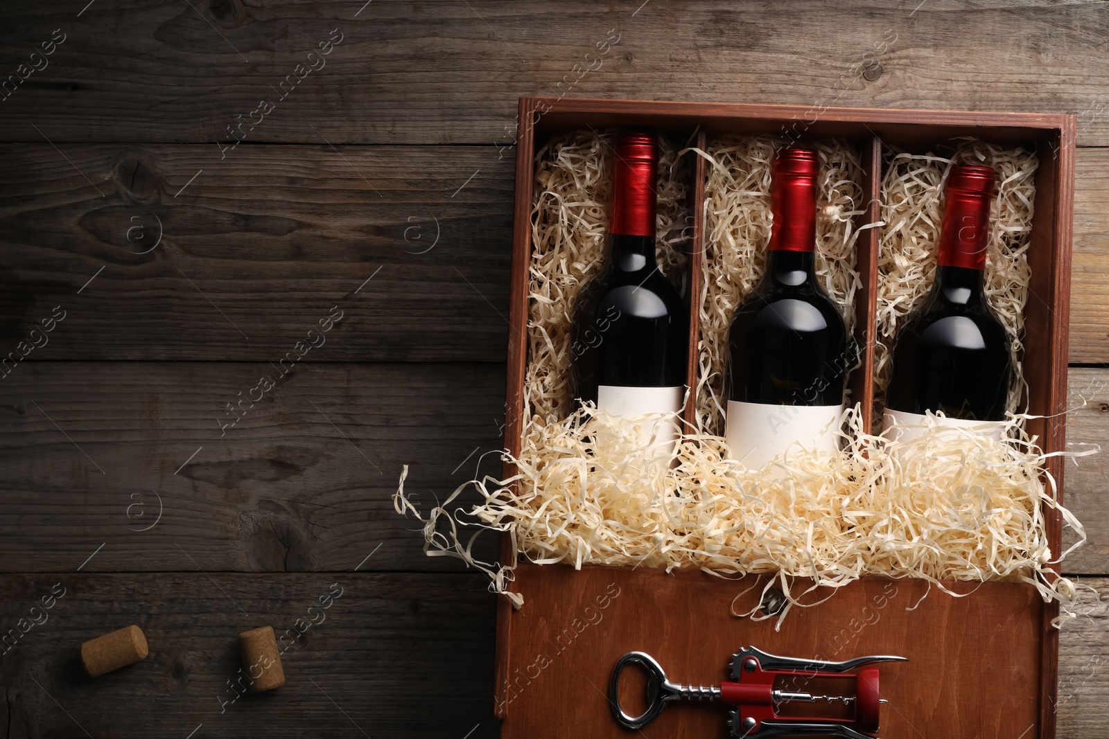 Photo of Box with wine bottles, corkscrew and corks on wooden table, flat lay. Space for text