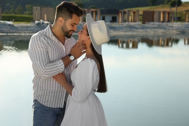 Photo of Romantic date. Beautiful couple spending time together near lake, space for text