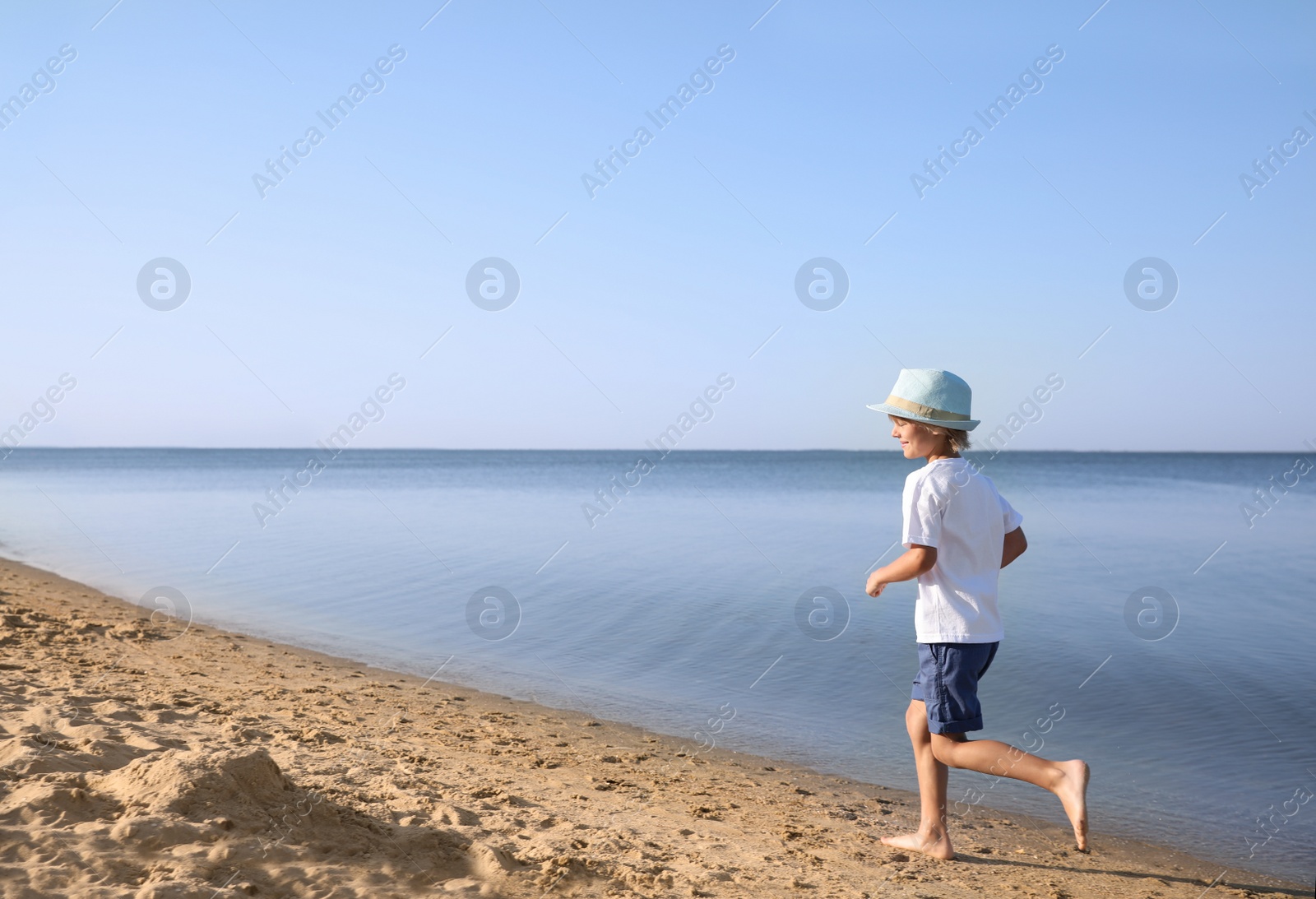 Photo of Cute little child running at sandy beach on sunny day