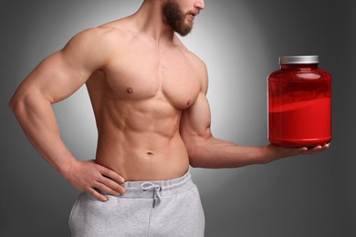 Young man with muscular body holding jar of protein powder on grey background, closeup