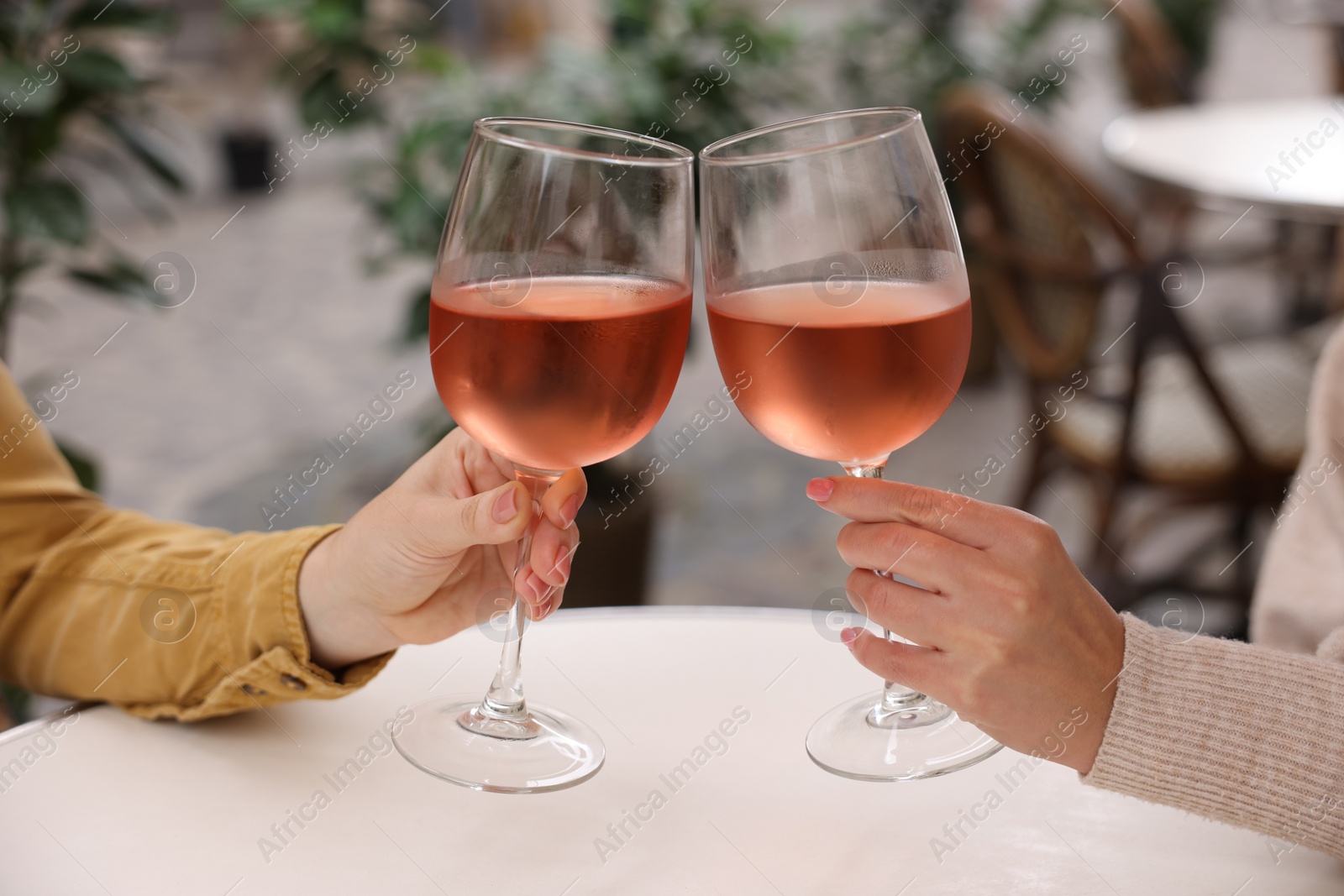 Photo of Women clinking glasses with rose wine at white table in outdoor cafe, closeup