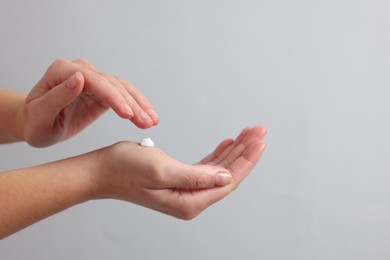 Woman applying cosmetic cream onto hand on light grey background, closeup. Space for text