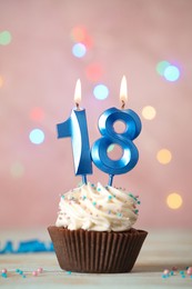 Photo of 18th birthday. Delicious cupcake with number shaped candles for coming of age party on white table