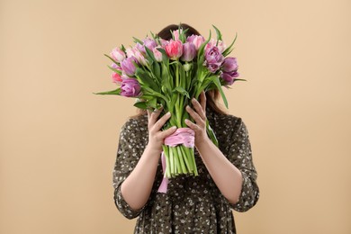 Photo of Young woman holding bouquet of beautiful tulips on beige background