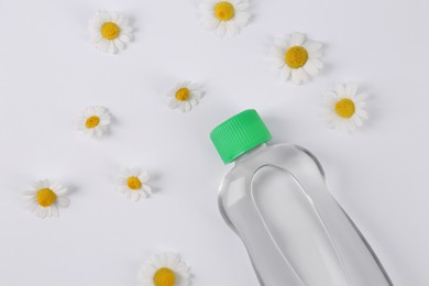 Photo of Transparent bottle with baby oil and daisies on white background, flat lay