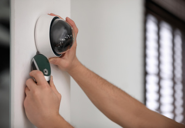 Photo of Technician installing CCTV camera on wall indoors, closeup