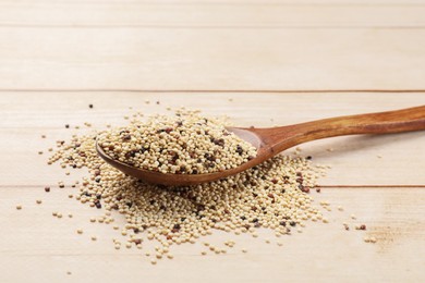 Photo of Spoon with raw quinoa seeds on wooden table, closeup