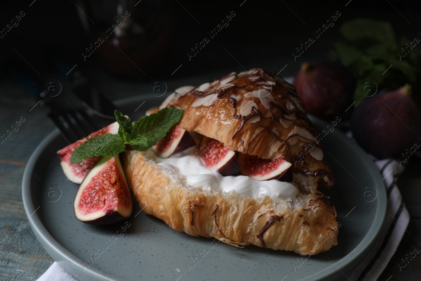 Photo of Delicious croissant with figs and cream on light blue wooden table, closeup