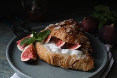 Delicious croissant with figs and cream on light blue wooden table, closeup