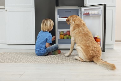 Little boy and cute Labrador Retriever seeking for food in refrigerator indoors