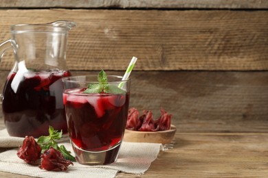 Photo of Delicious iced hibiscus tea, mint and dry flowers on wooden table, space for text