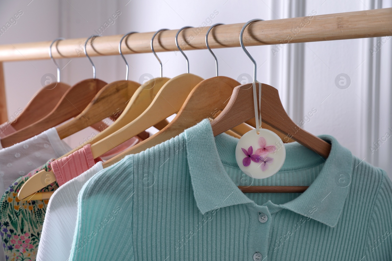 Photo of Beautiful scented wax sachet and clothes hanging on wooden rack indoors