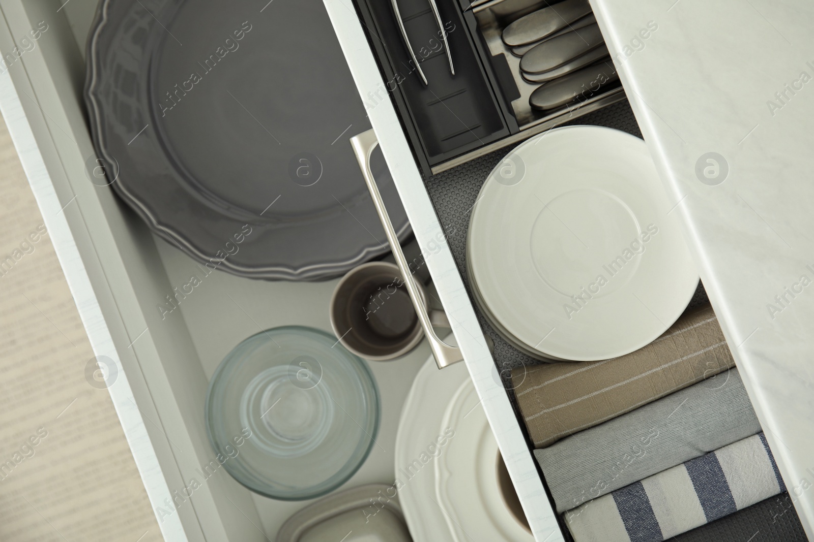 Photo of Open drawers of kitchen cabinet with different dishware and towels, top view