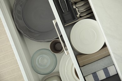 Open drawers of kitchen cabinet with different dishware and towels, top view