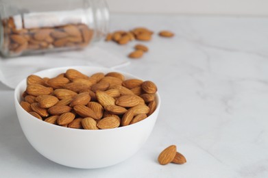 Photo of Bowl of delicious almonds on white marble table. Space for text