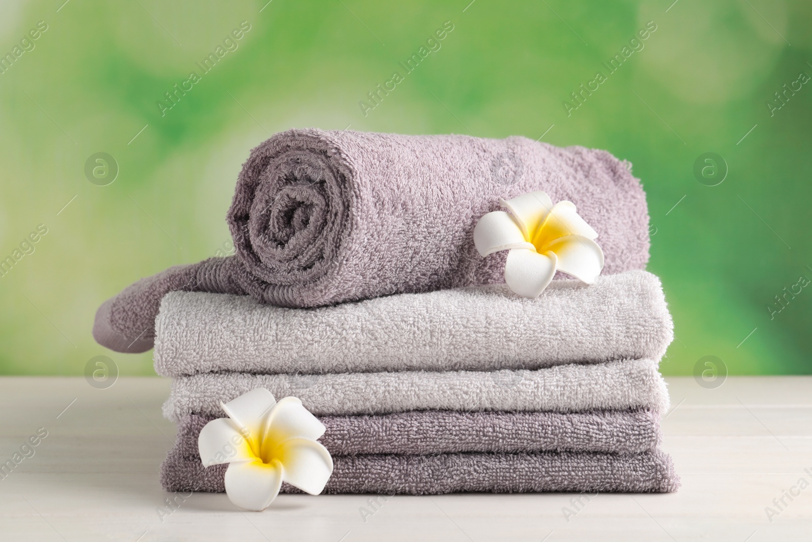 Photo of Soft folded towels and plumeria flowers on white wooden table