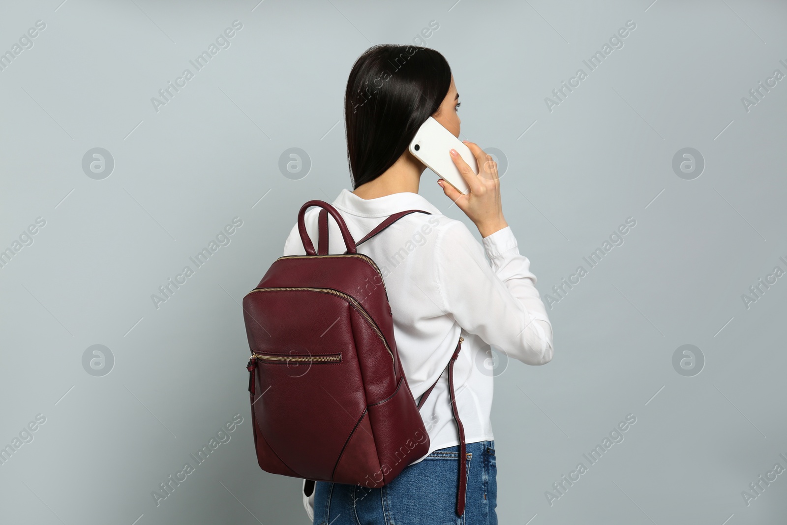 Photo of Young woman with stylish backpack talking on phone against light grey background, back view