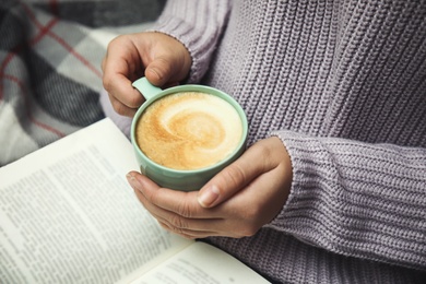 Woman with cup of coffee reading book at home, closeup