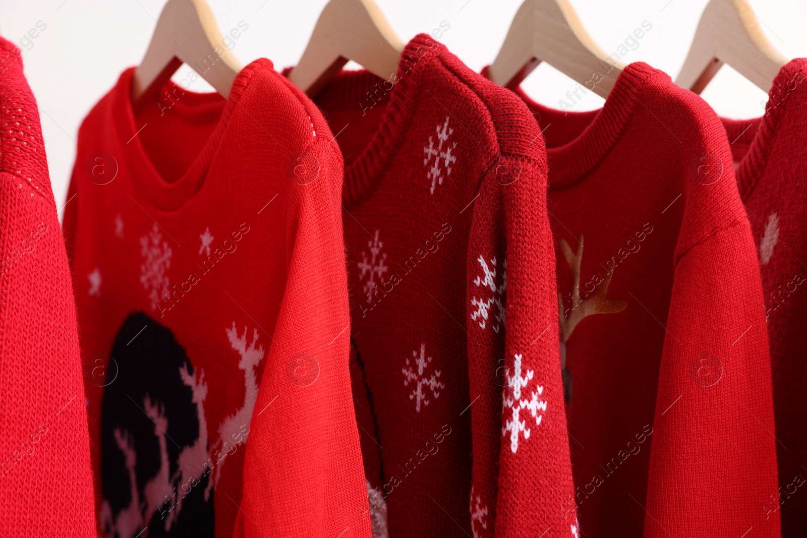 Photo of Different Christmas sweaters hanging on rack against white background, closeup