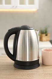 Photo of Modern electric kettle and cup on table in kitchen