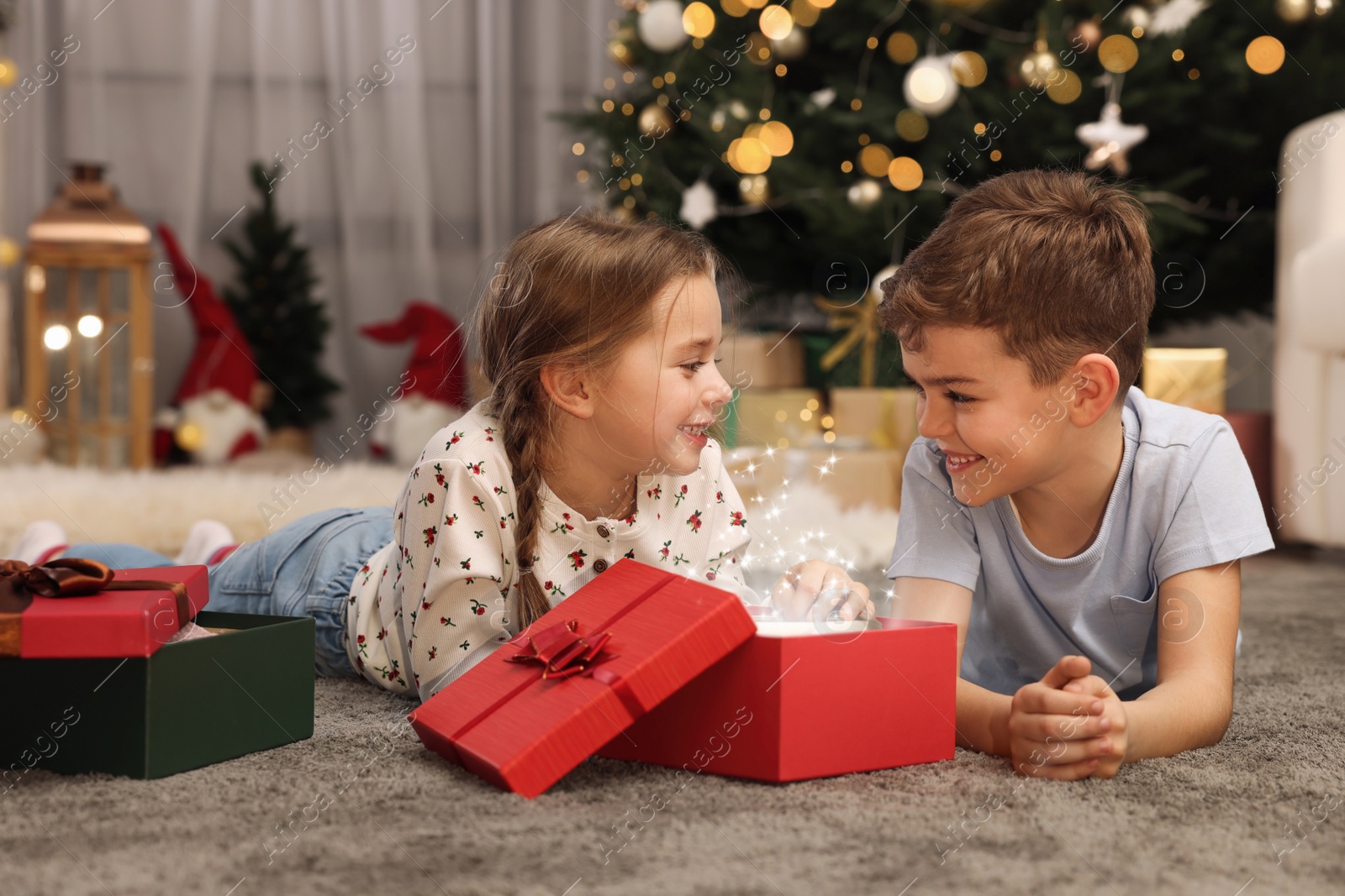 Photo of Cute little children opening gift box near Christmas tree at home