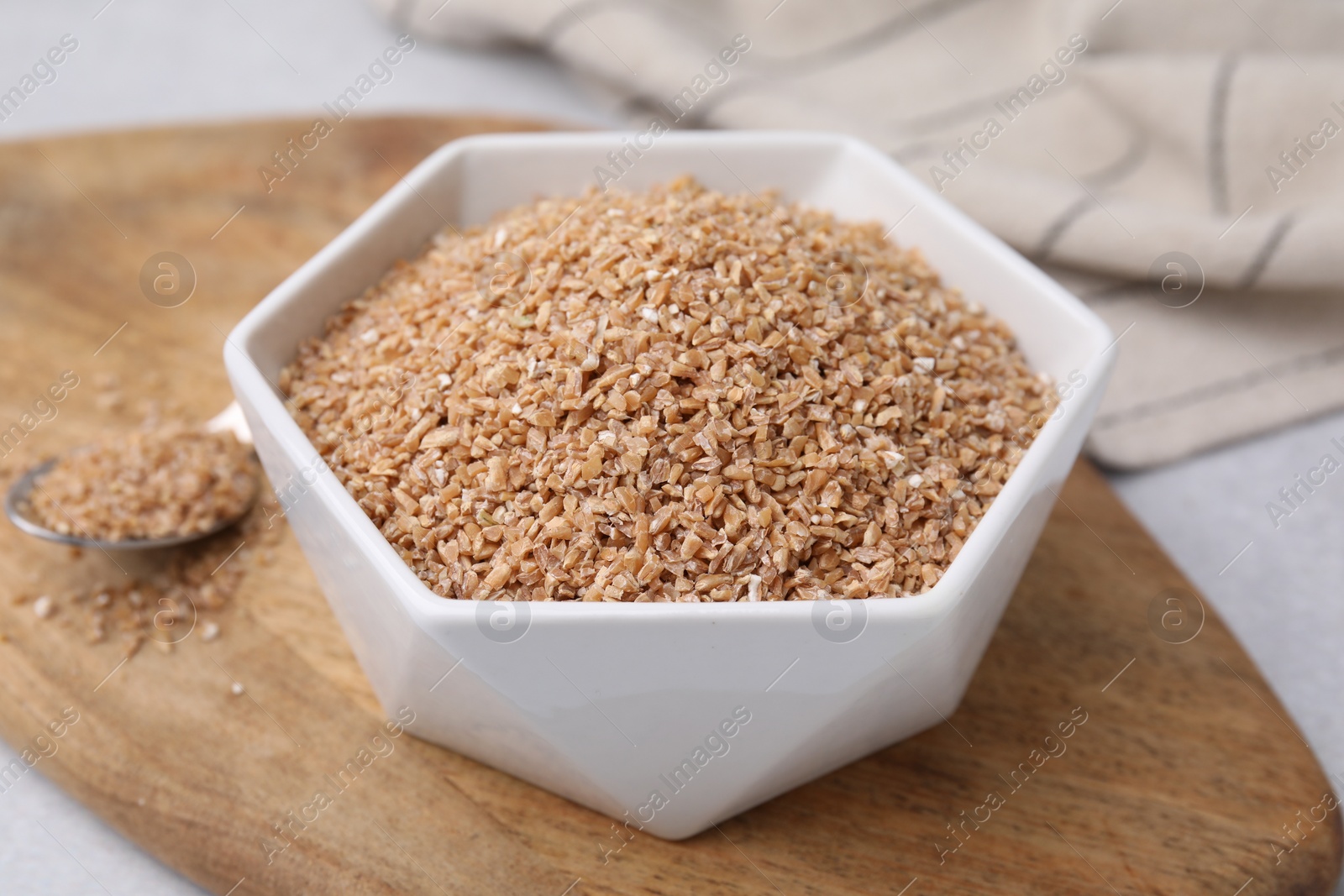 Photo of Dry wheat groats in bowl on light table, closeup