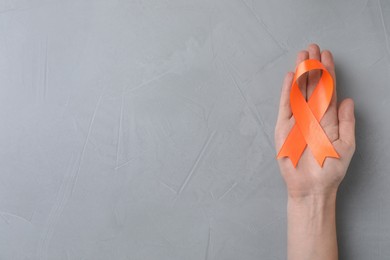 Photo of Man holding orange ribbon on light grey background, top view with space for text. Multiple sclerosis awareness