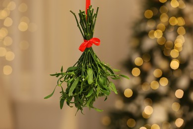 Photo of Mistletoe bunch with red bow on blurred background, bokeh effect. Traditional Christmas decor