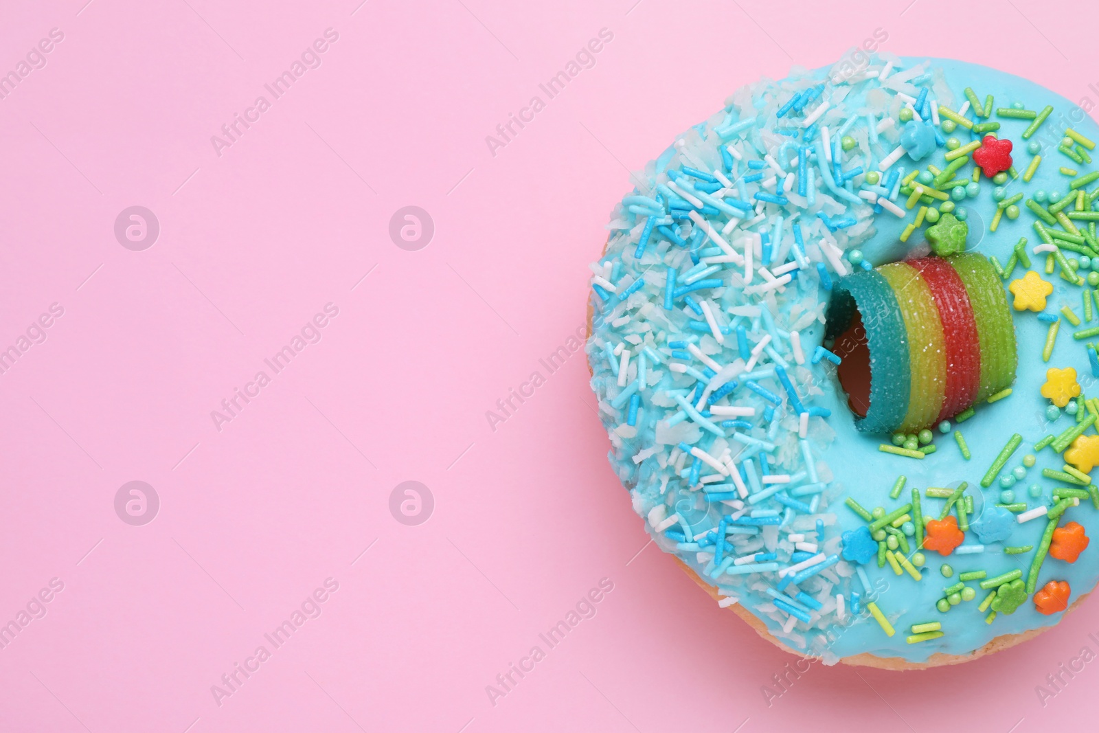 Photo of Glazed donut decorated with sprinkles on pink background, top view. Space for text. Tasty confectionery