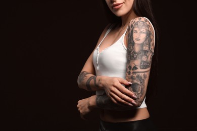 Photo of Beautiful woman with tattoos on arms against black background, closeup. Space for text