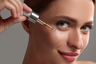 Photo of Beautiful young woman applying cosmetic serum onto her face on grey background, closeup