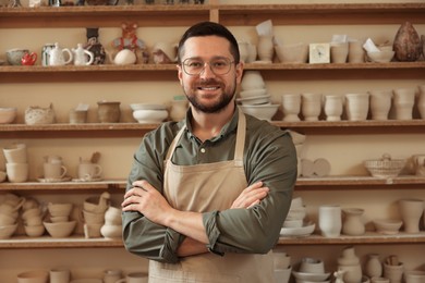 Photo of Portrait of smiling craftsman near shelf with different pottery in workshop