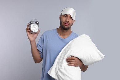 Photo of Tired man with pillow, sleep mask and alarm clock on light grey background. Insomnia problem
