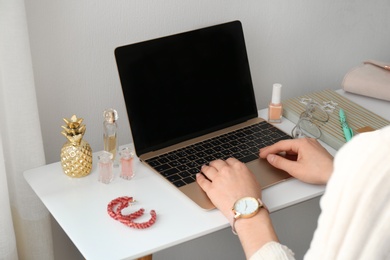 Woman with cosmetic products using laptop at table, closeup. Beauty blogger