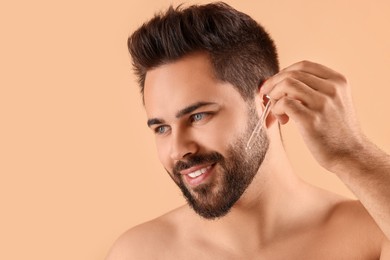Photo of Handsome man applying cosmetic serum onto face on beige background, space for text