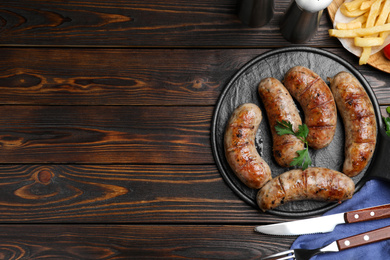 Tasty grilled sausages served on wooden table, flat lay. Space for text