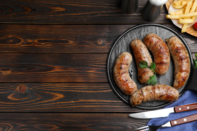 Photo of Tasty grilled sausages served on wooden table, flat lay. Space for text