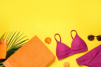 Beach towel, swimsuit, sunglasses and sun protection product on yellow background, flat lay. Space for text