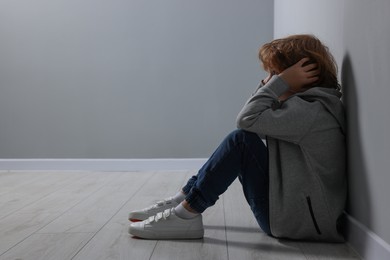 Photo of Child abuse. Upset boy sitting on floor near grey wall, space for text