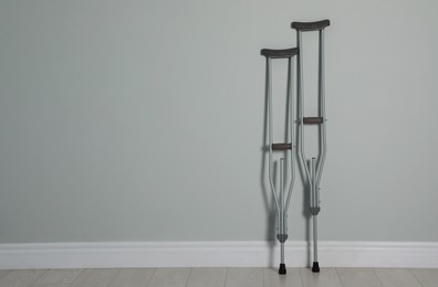 Photo of Pair of axillary crutches near light grey wall. Space for text