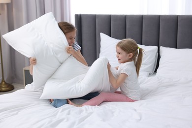 Cute little sisters having pillow fight on bed at home