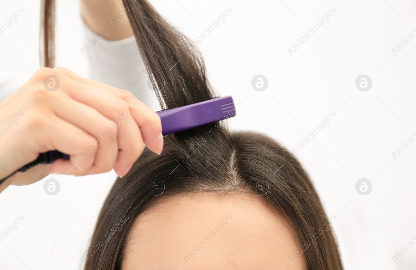 Photo of Hairdresser using modern flat iron to style client's hair in salon, closeup