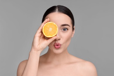 Photo of Beautiful young woman with piece of orange on grey background