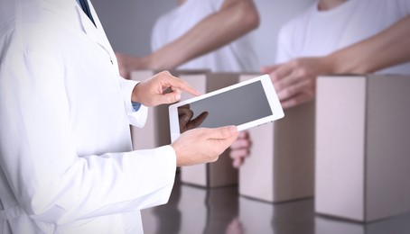 Production line. Manager using tablet while workers folding cardboard boxes, closeup